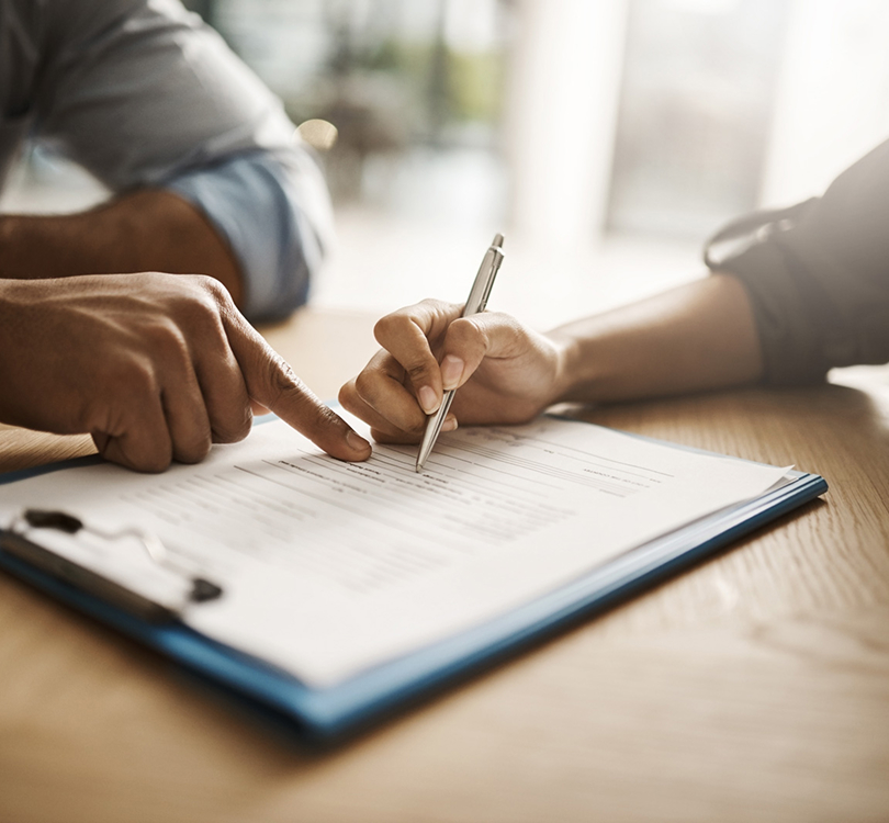 Person signing document while another points at form