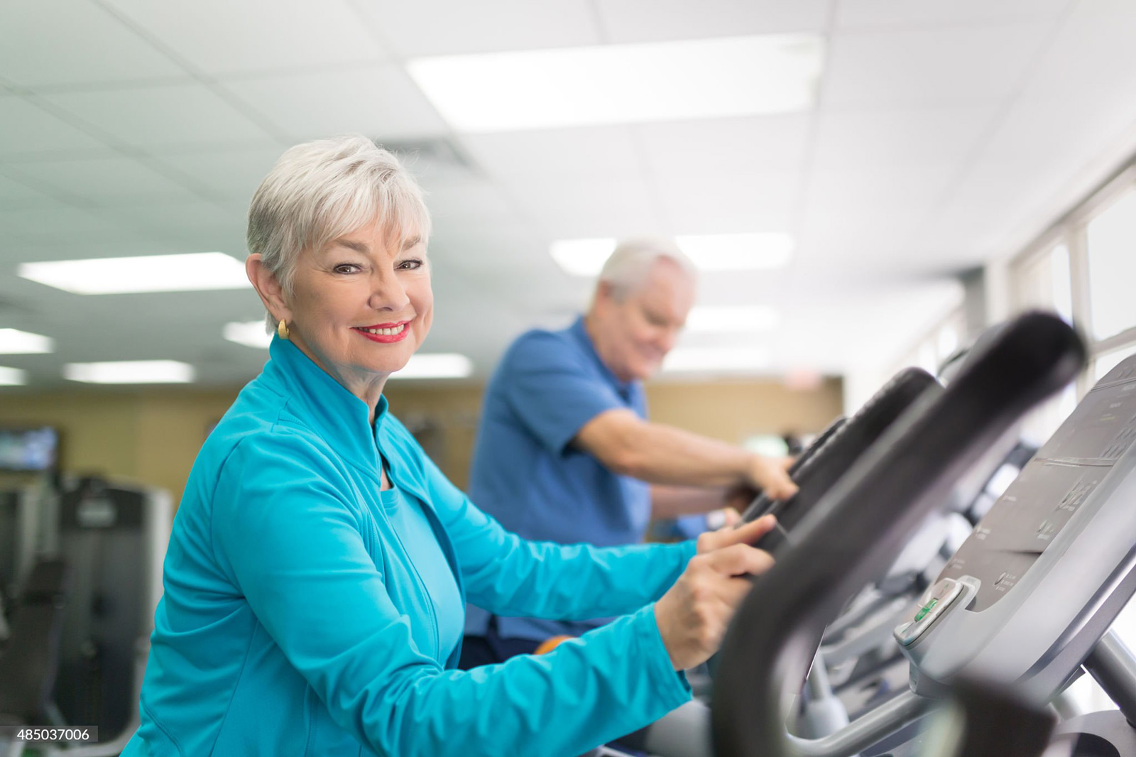 Senior woman smiling while using treadmill at gym