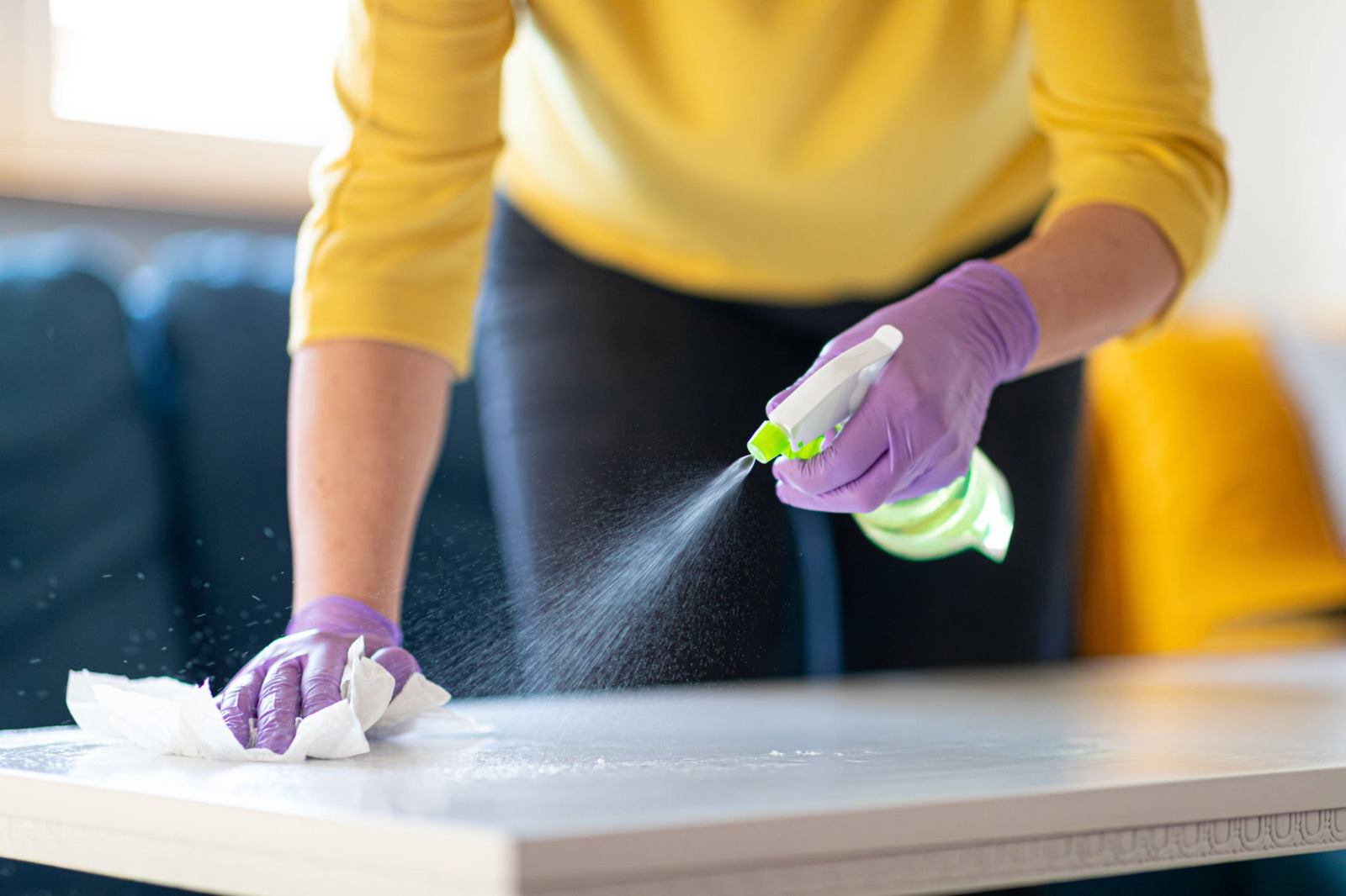 Person disinfecting table with spray and cloth