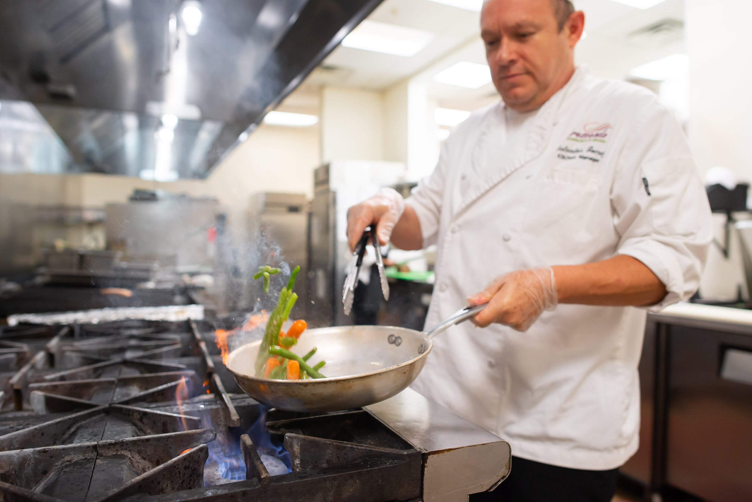 Chef sautéing vegetables in pan over gas stove