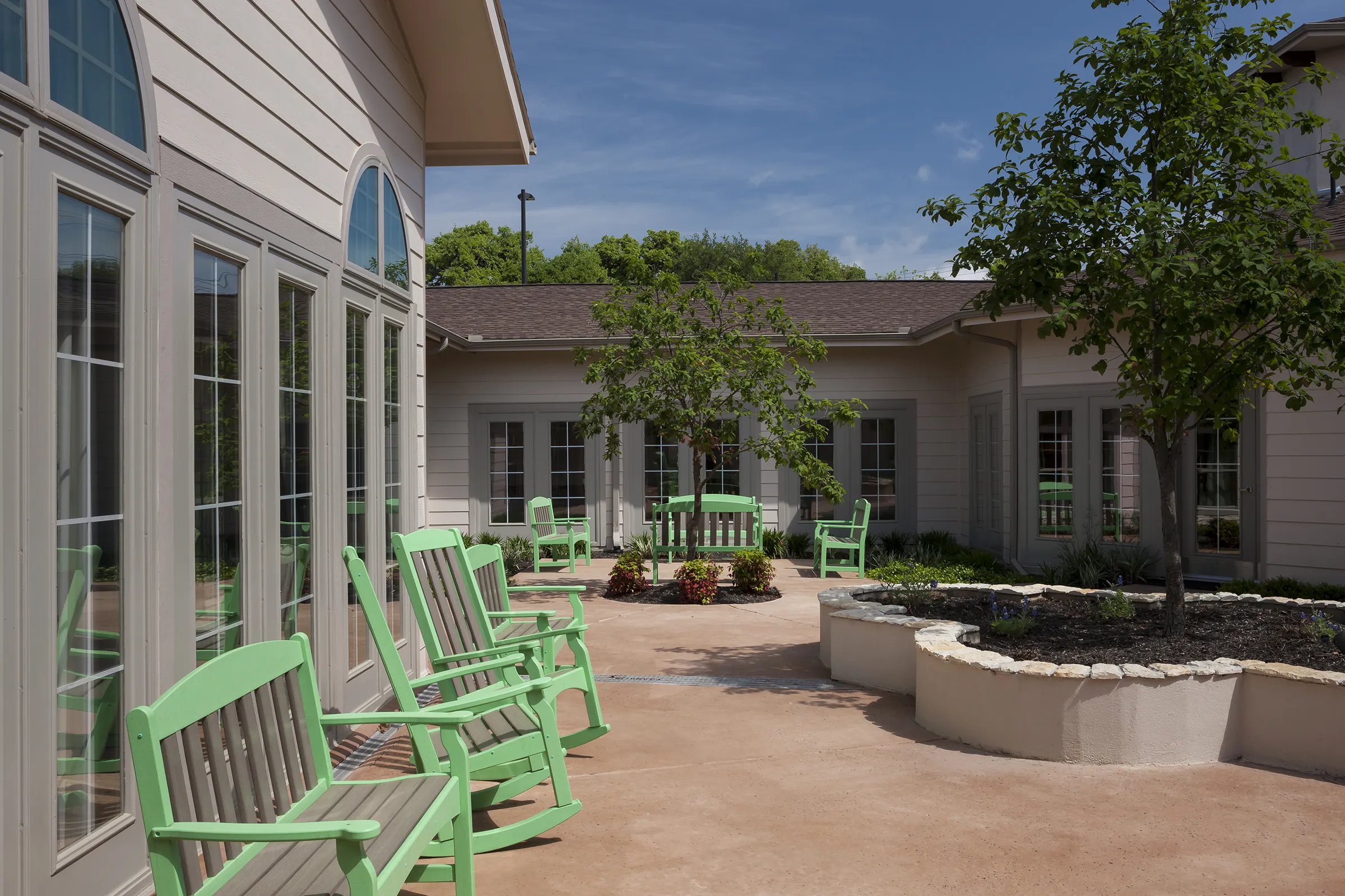 Sunny courtyard with green rocking chairs and trees