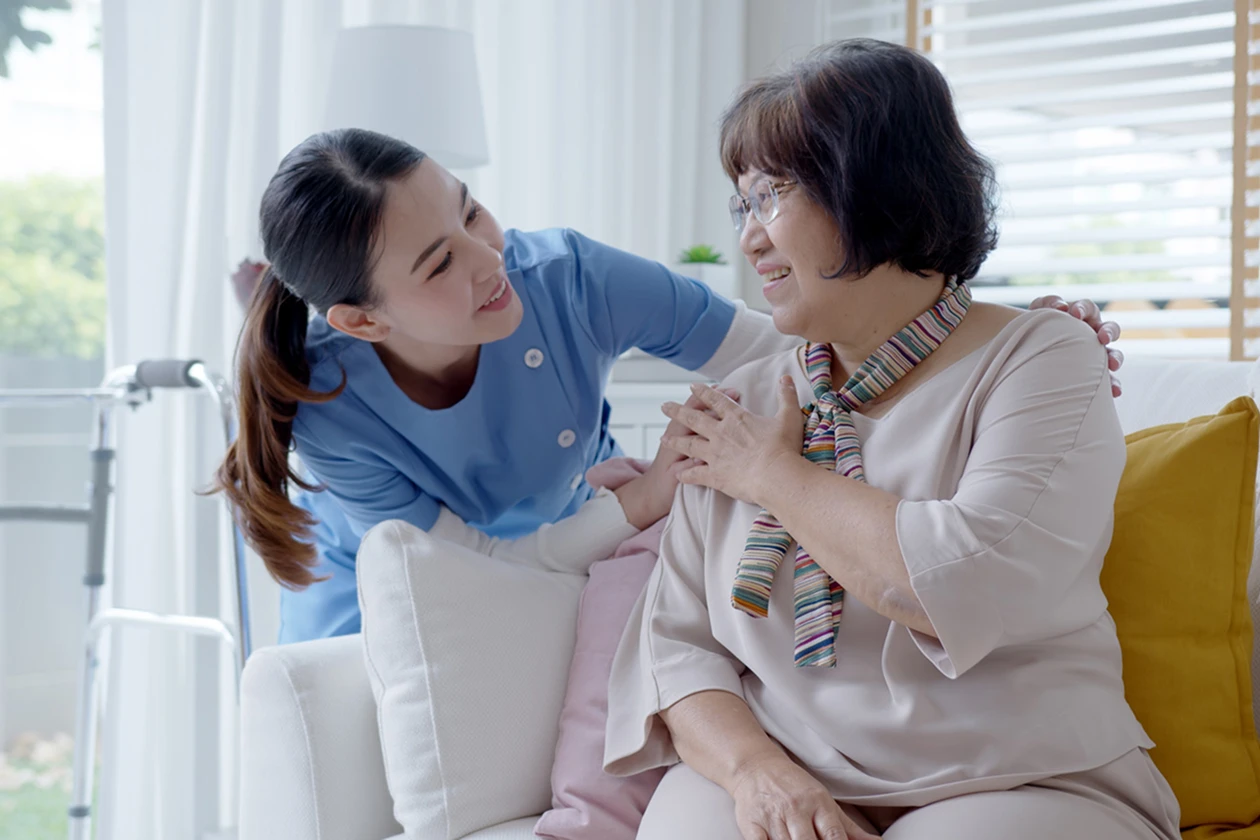 Caregiver comforting elderly woman on living room couch